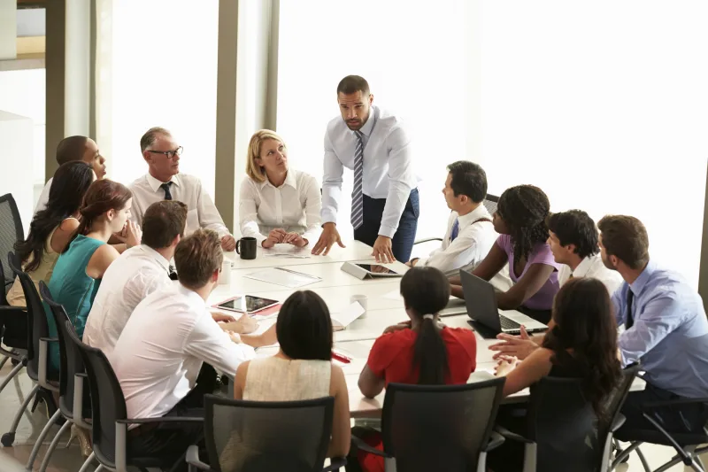 A diverse group seated around a boardroom table in discussion.